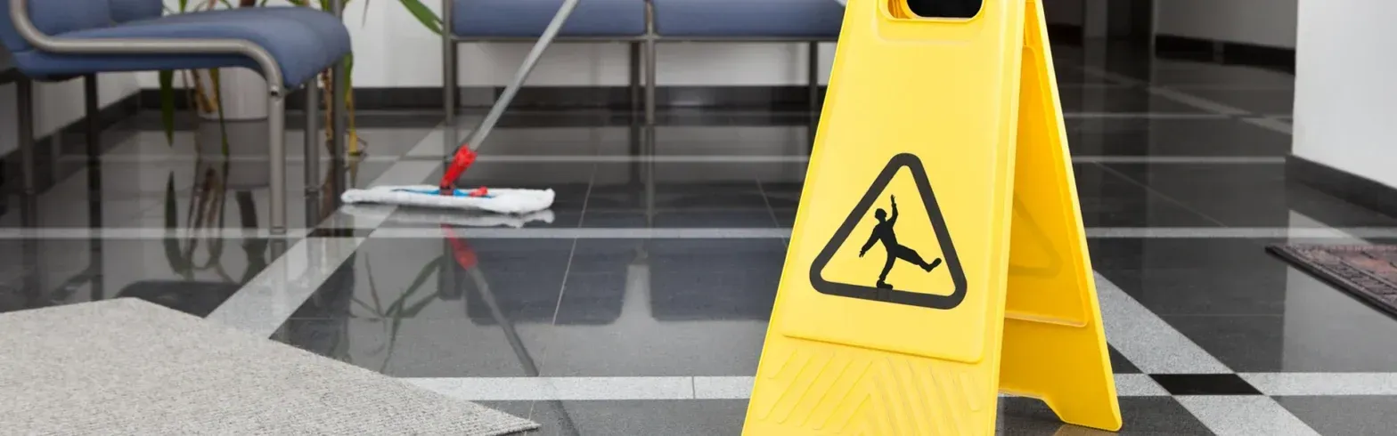 Yellow caution wet floor sign on a shiny tiled indoor floor with spilled water and chairs in the background