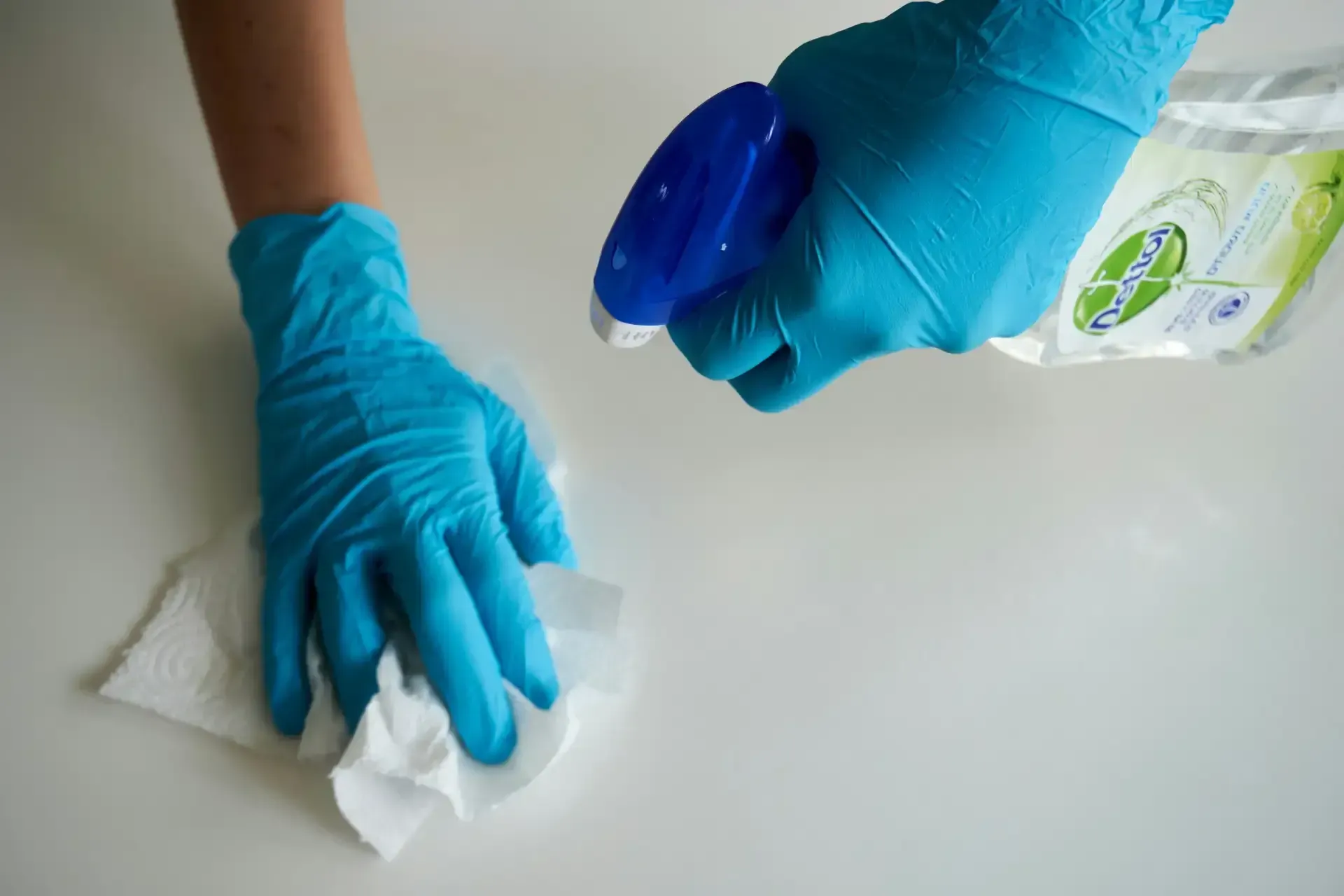 Cleaner sanitizing a high-touch surface with disinfectant spray and a microfiber cloth while wearing protective gloves.