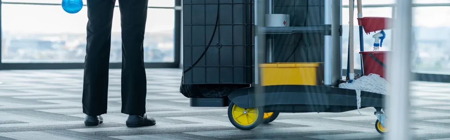 Man pushing a luggage cart with a yellow suitcase in an airport terminal near large windows