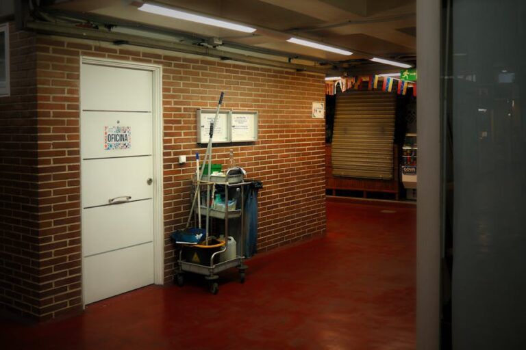 Brick hallway with red floor, white door, utility cart, and a closed shutter at the end.