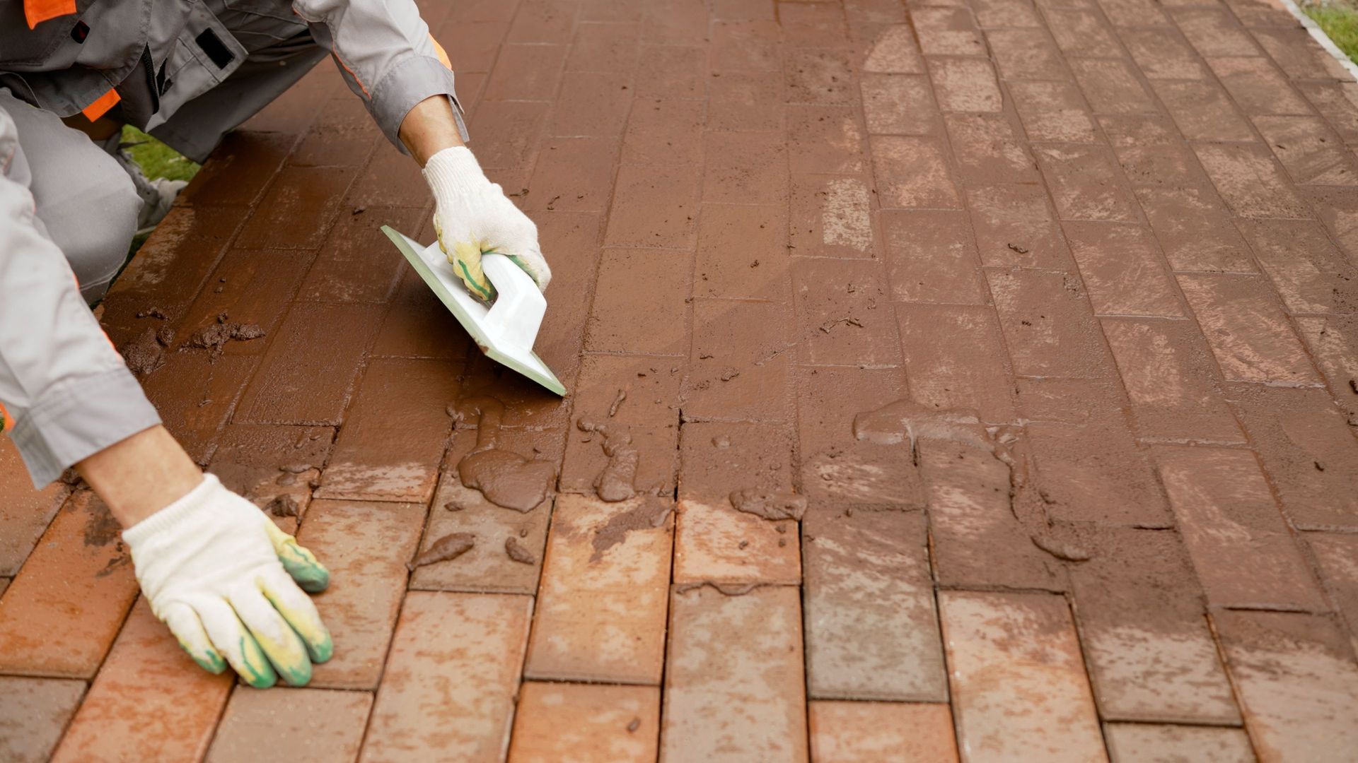 Worker scrubbing muddy brick pavement with a trowel and gloves Worker scrubbing muddy brick pavement with a trowel and gloves