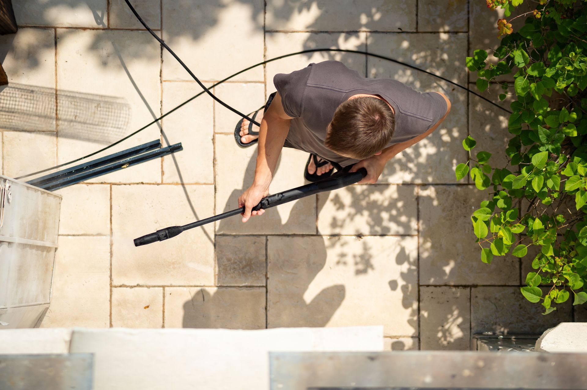 Person sweeping a stone patio with a broom, viewed from above, with cords and green leaves nearby Person sweeping a stone patio with a broom, viewed from above, with cords and green leaves nearby