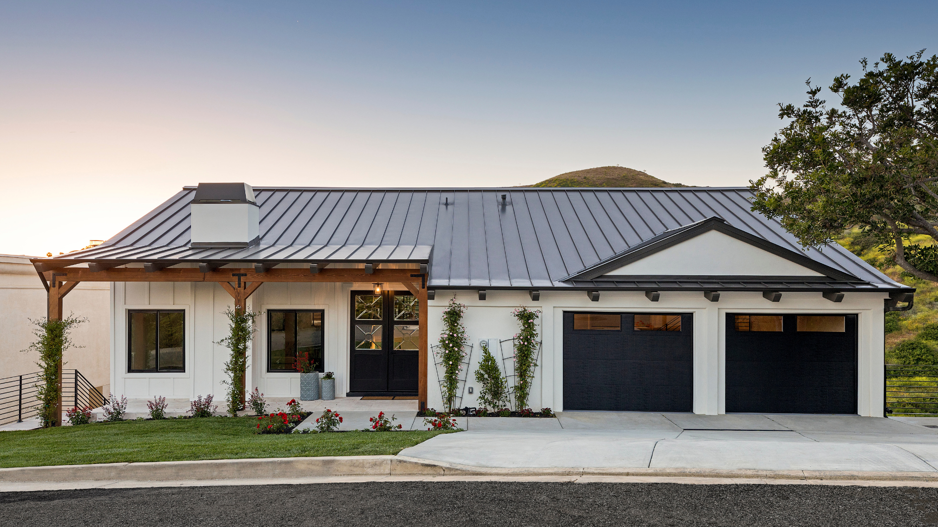 A white house with a black roof and black garage doors