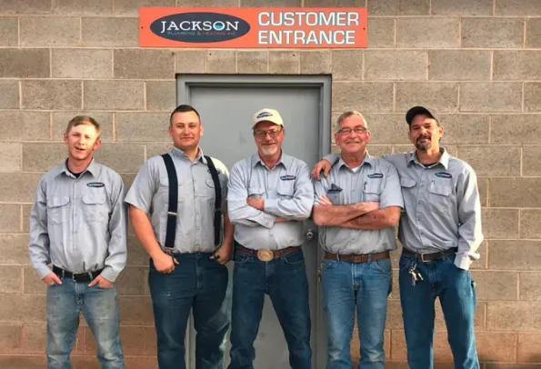 A group of men are posing for a picture in front of a jackson customer entrance sign.