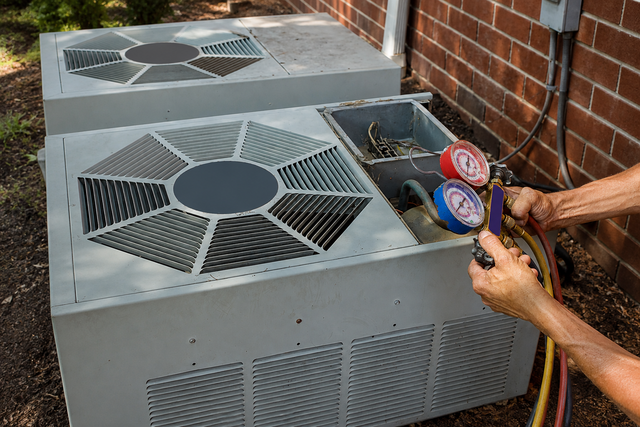 Technician testing rooftop HVAC unit with gauges beside a brick wall