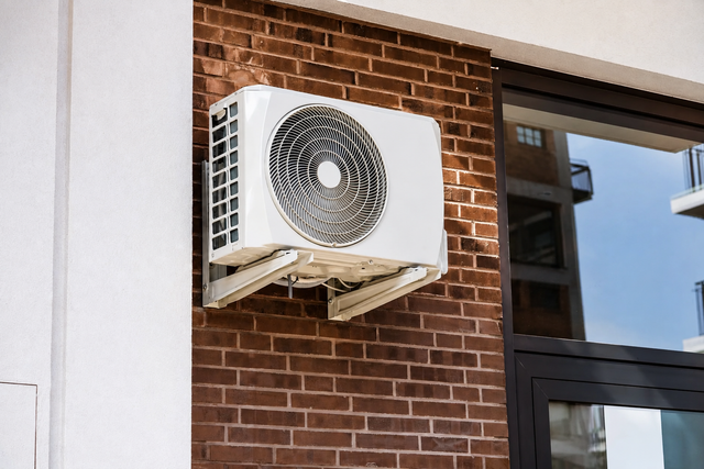 White wall-mounted air conditioner on a brick exterior wall beside a window