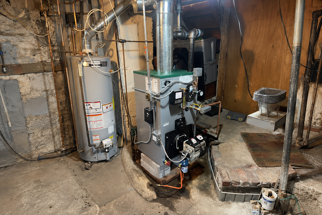 Basement utility area with furnace, water heater, and exposed pipes beside concrete walls.