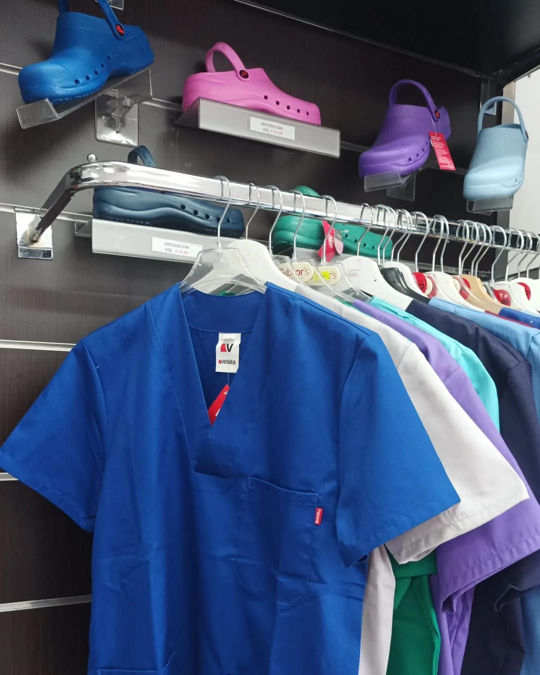 Una casacca blu da infermiere appesa a uno scaffale, con sopra esposte delle scarpe colorate.