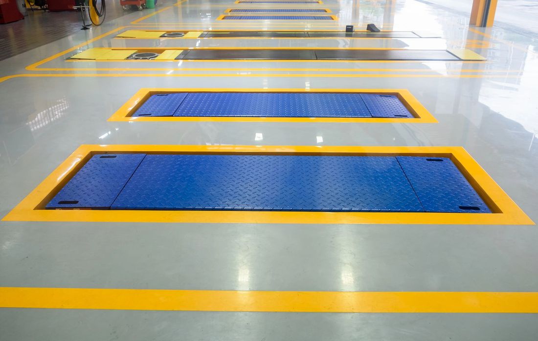 Pavimento industriale interno con due griglie metalliche blu delineate con vernice gialla.