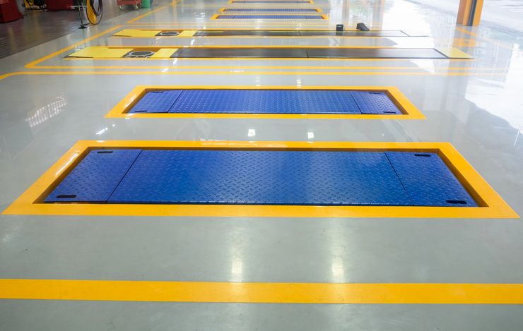 Pavimento industriale interno con due griglie metalliche blu delineate con vernice gialla.
