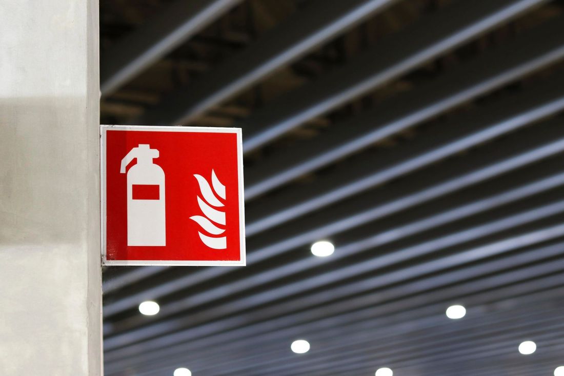Cartello rosso di un estintore su un pilastro di cemento in un parcheggio coperto.