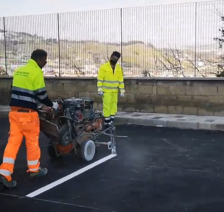 Due operai con abbigliamento ad alta visibilità usano una macchina per la segnaletica orizzontale su una strada appena asfaltata.