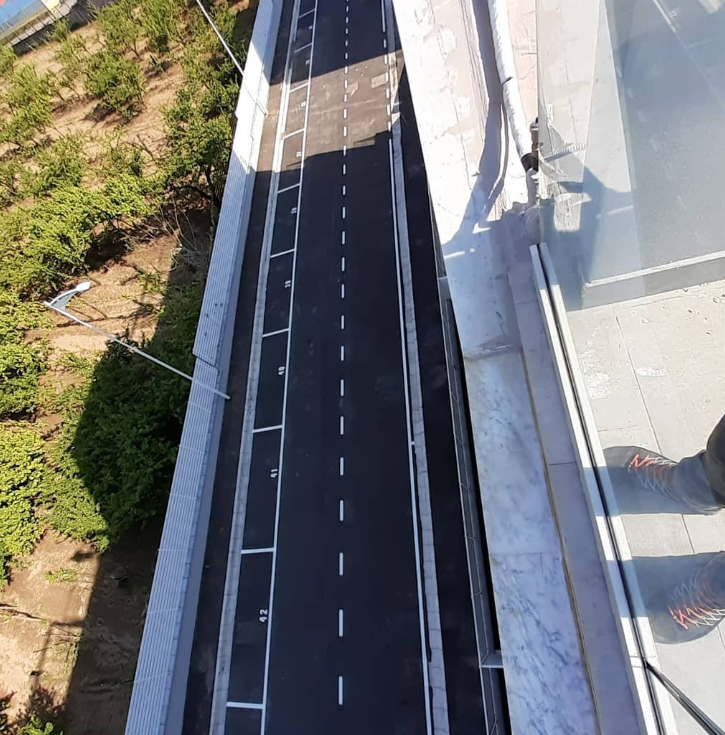 Vista aerea di una strada nera appena asfaltata accanto a un edificio bianco e ad alcuni alberi