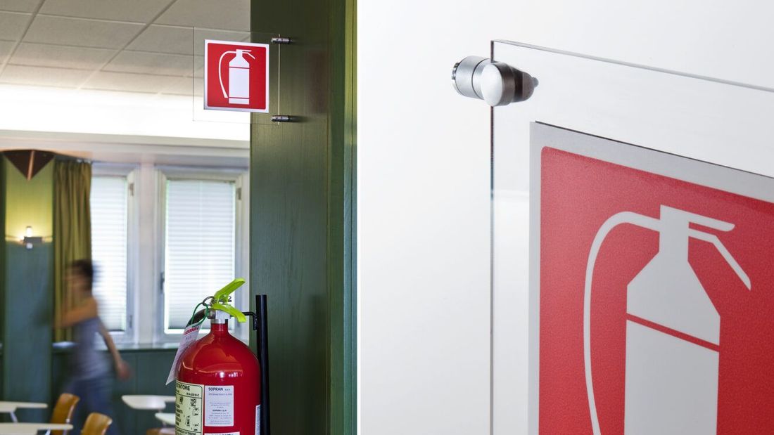 Corridoio dell'ufficio con cartello rosso di estintore e estintore vicino a un corridoio con finestre.