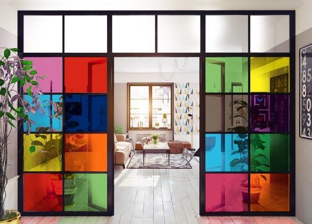 Porte colorate in stile vetrata incorniciano un luminoso soggiorno con divano sullo sfondo.