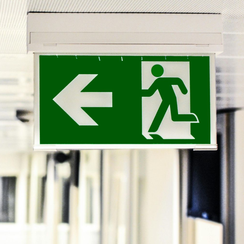 Cartello verde di uscita di emergenza con freccia a sinistra appeso in un corridoio