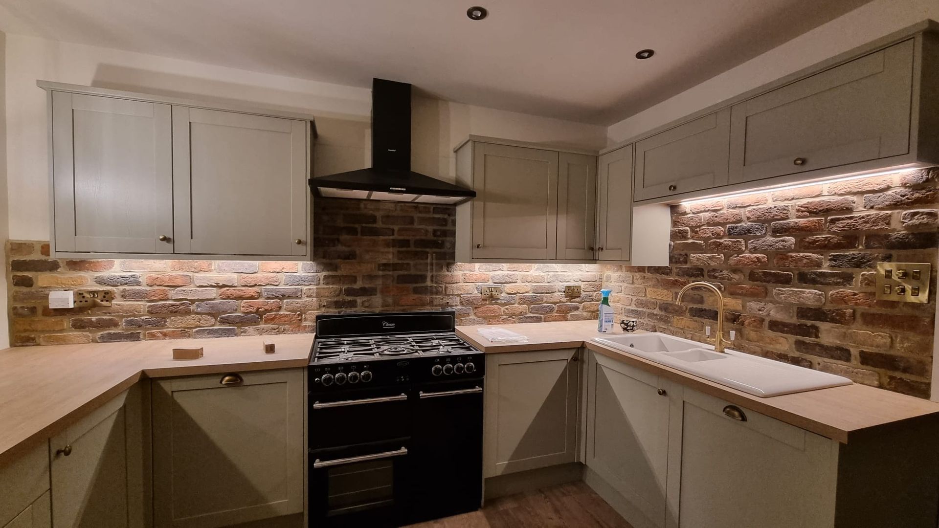 A new sage kitchen with exposed brick backlash, gold accents and black appliances
