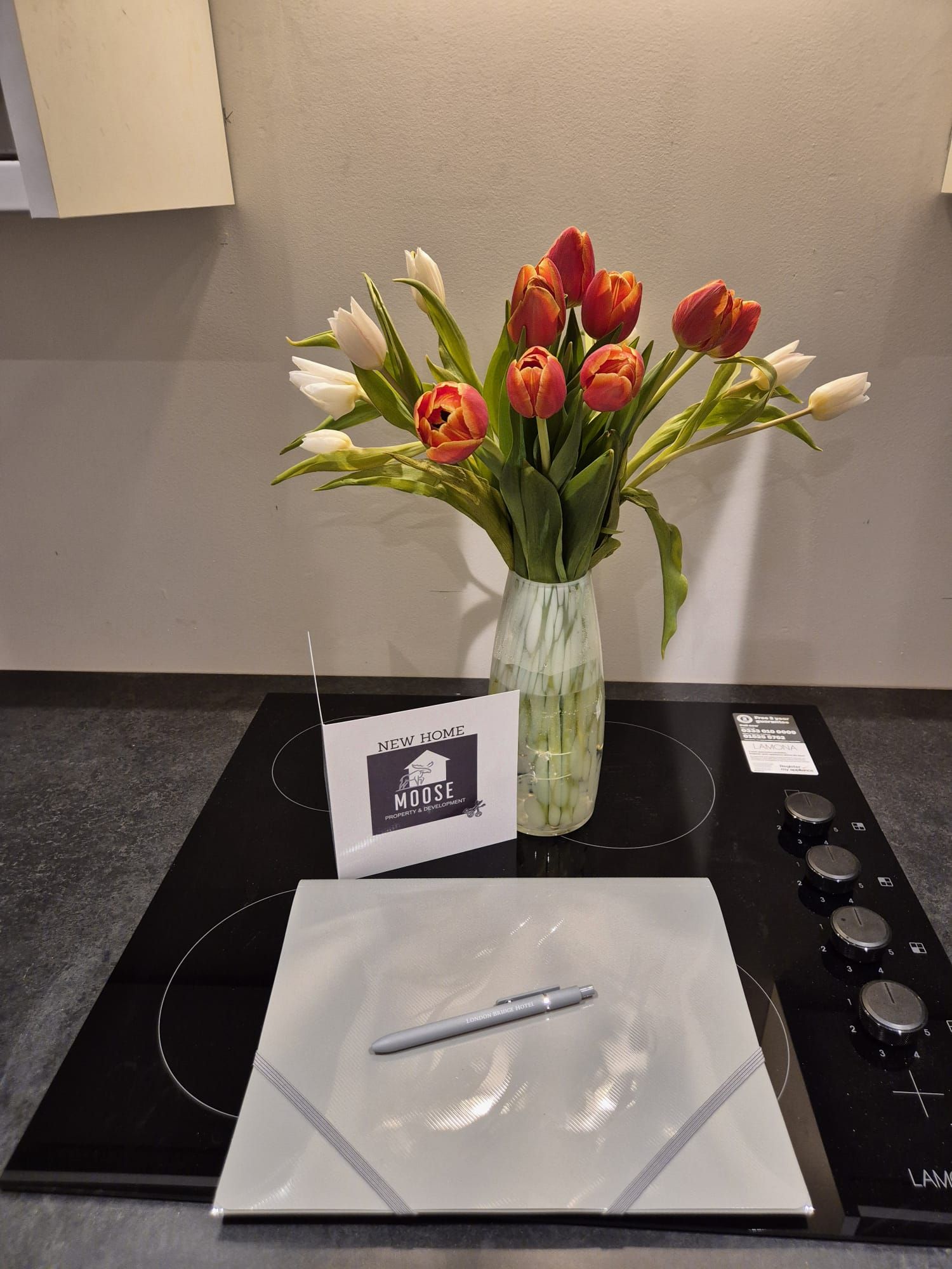 A vase of red and white tulips on a kitchen counter beside a card and notepad.