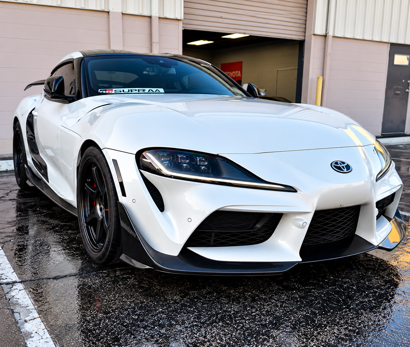 White sports car parked outside a garage on wet pavement