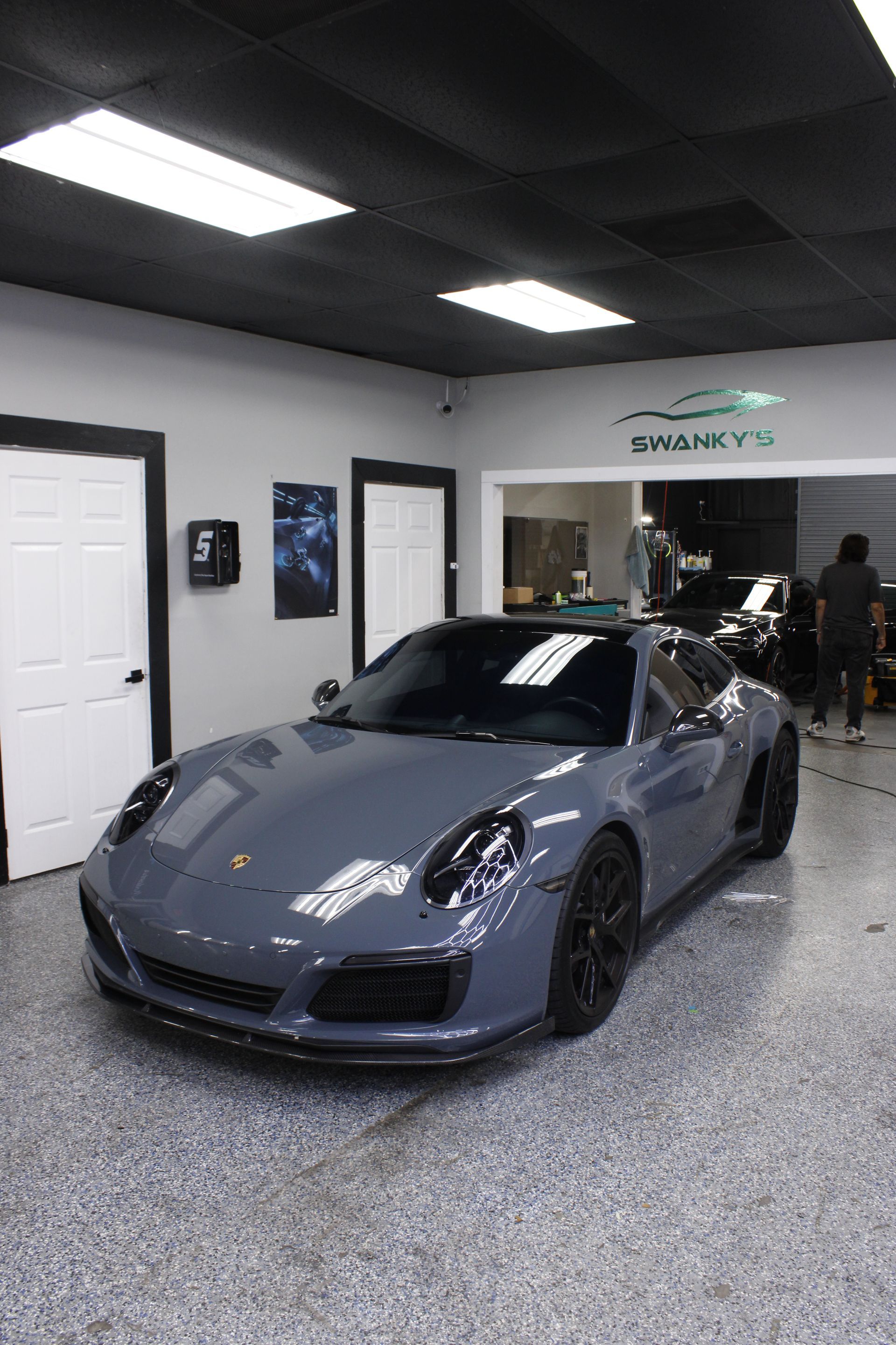 Gray sports car in a garage showroom with black ceiling lights and white walls