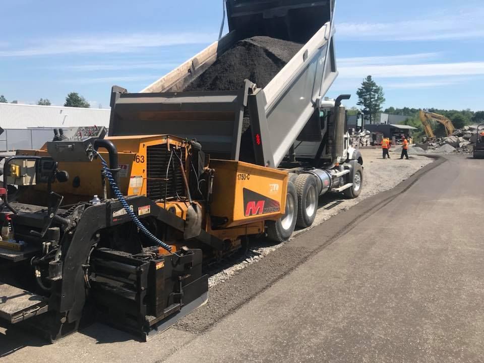 Finisseur d'asphalte et camion-benne à l'œuvre sur un chantier routier, des ouvriers à proximité