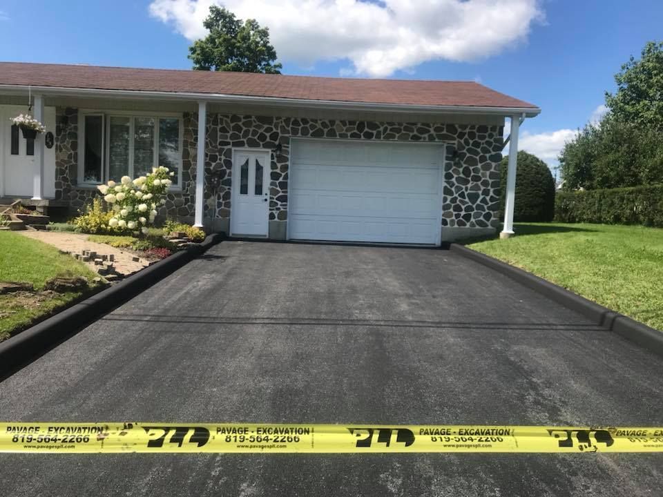 Maison de banlieue avec une allée noire fraîchement pavée, du ruban de signalisation jaune devant et un garage.