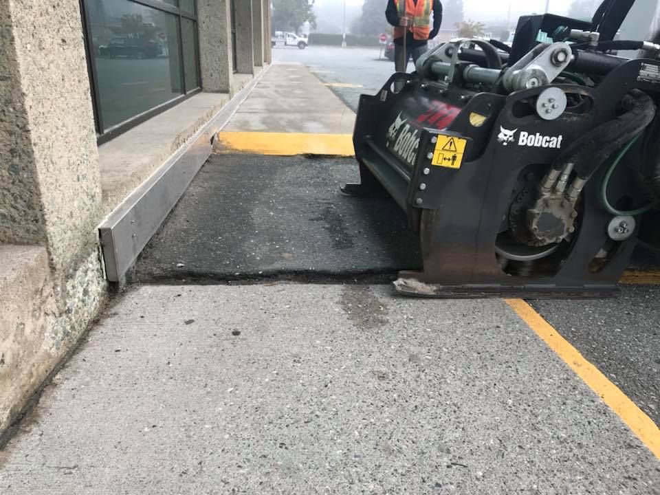 Petite chargeuse compacte avec rampe se déployant sur un trottoir près de l'entrée d'un bâtiment.