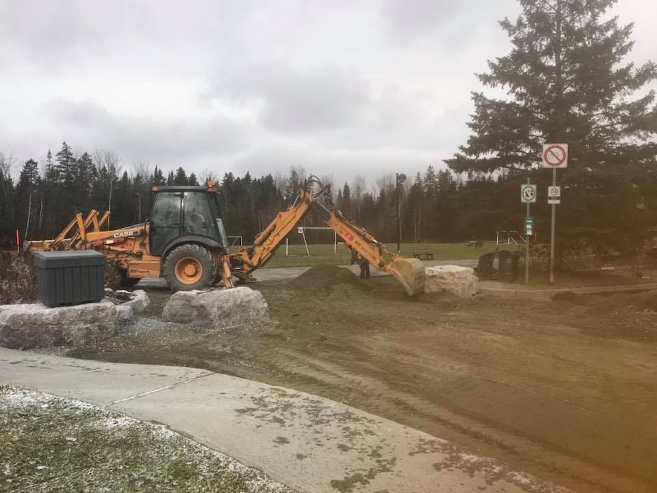 Une chargeuse-pelleteuse travaille sur un bord de route boueux près d'une forêt et de panneaux de signalisation de chantier.