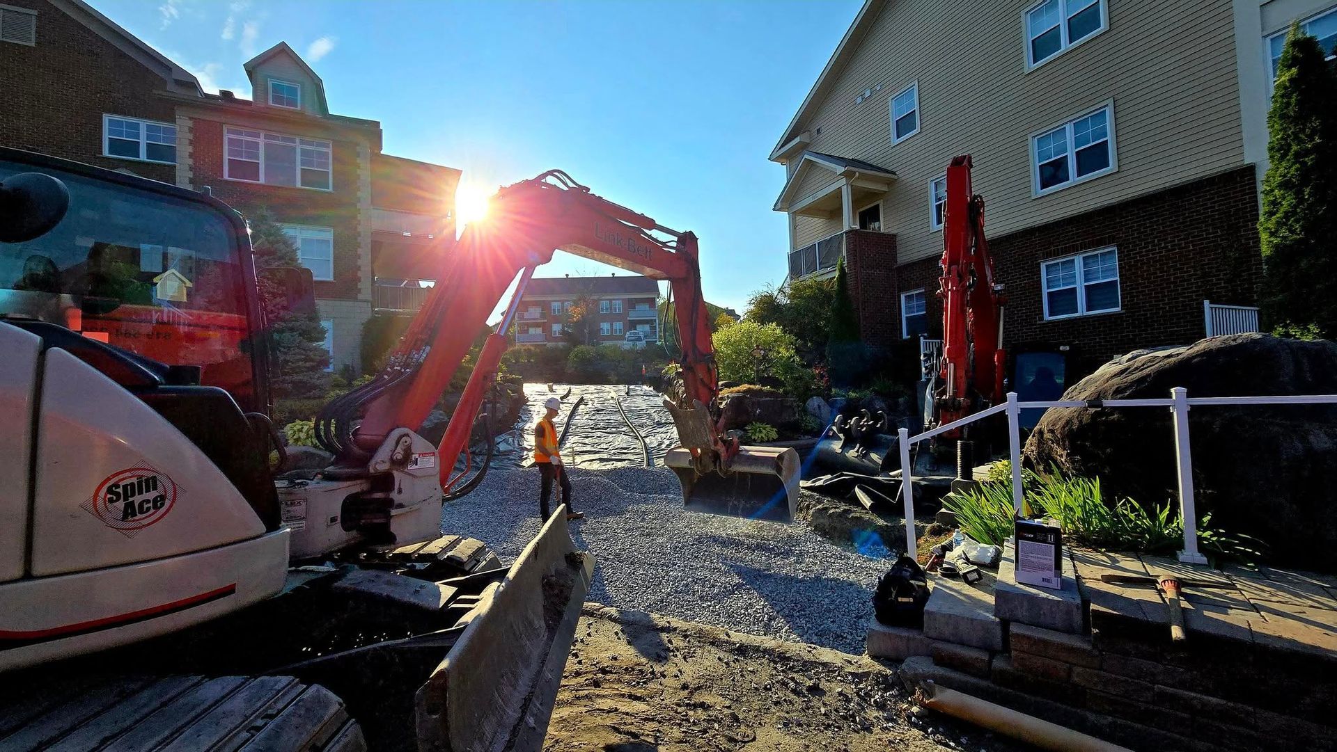Chantier de construction avec une pelleteuse rouge soulevant des gravats entre des immeubles d'habitation sous un soleil éclatant.