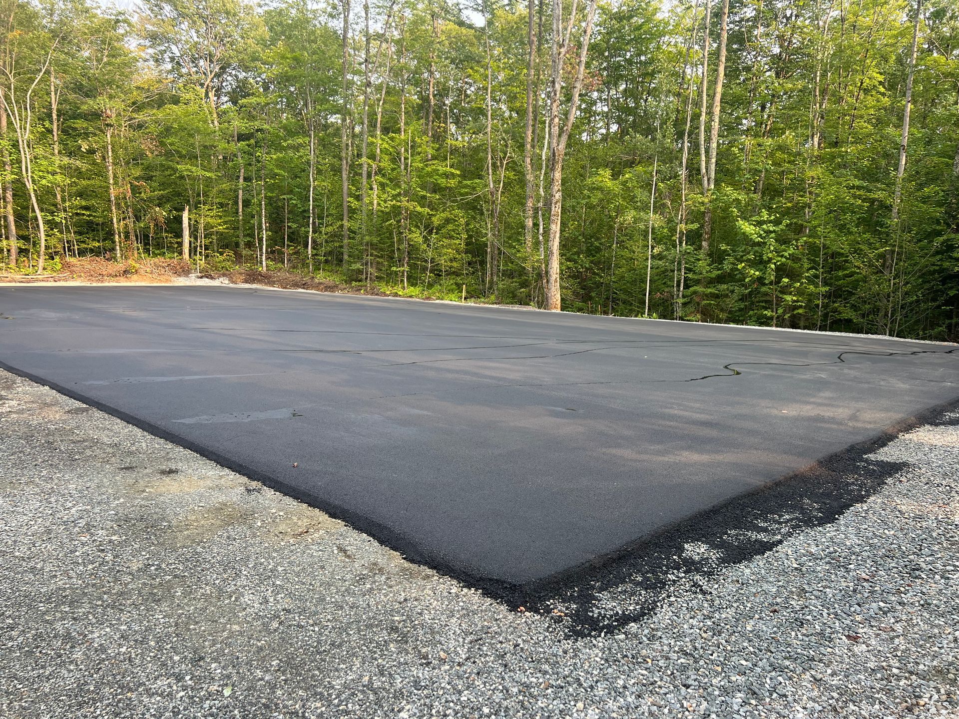 Surface asphaltée fraîchement pavée à côté de gravier dans une zone boisée