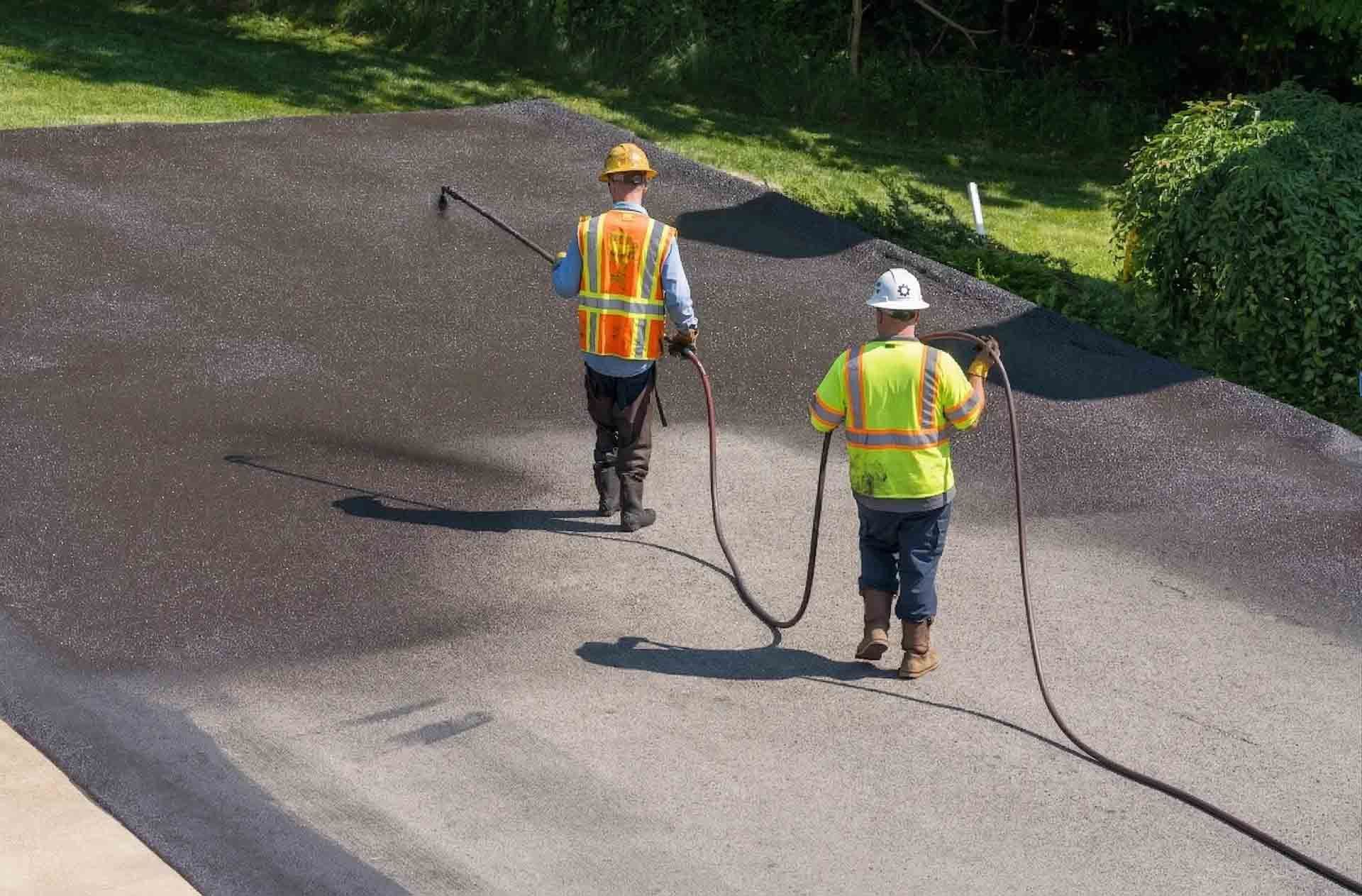 Deux ouvriers portant des gilets de sécurité pavant une route avec des rouleaux compresseurs d'asphalte chaud