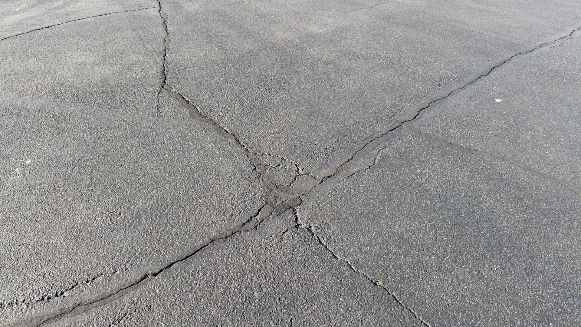 Revêtement d'asphalte gris fissuré avec des fissures entrecroisées
