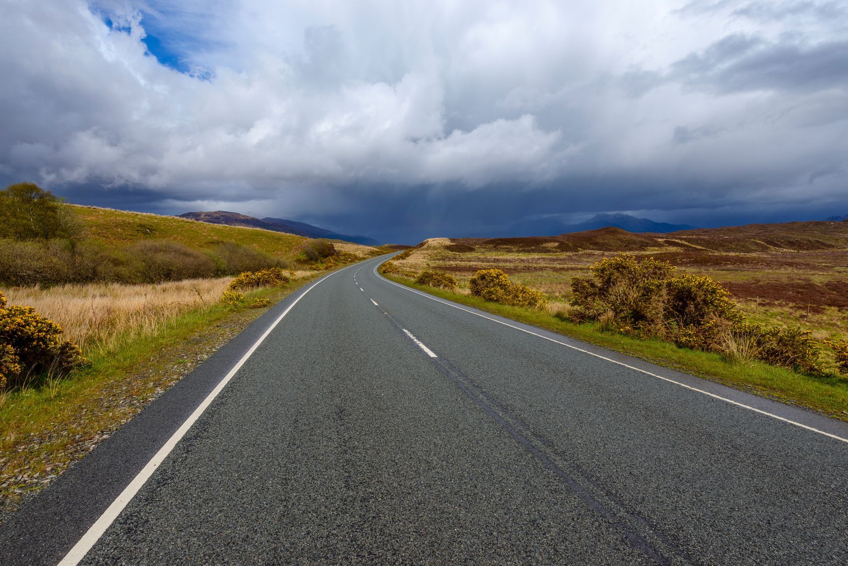 Route sinueuse et déserte sous un ciel nuageux dramatique dans un paysage rural