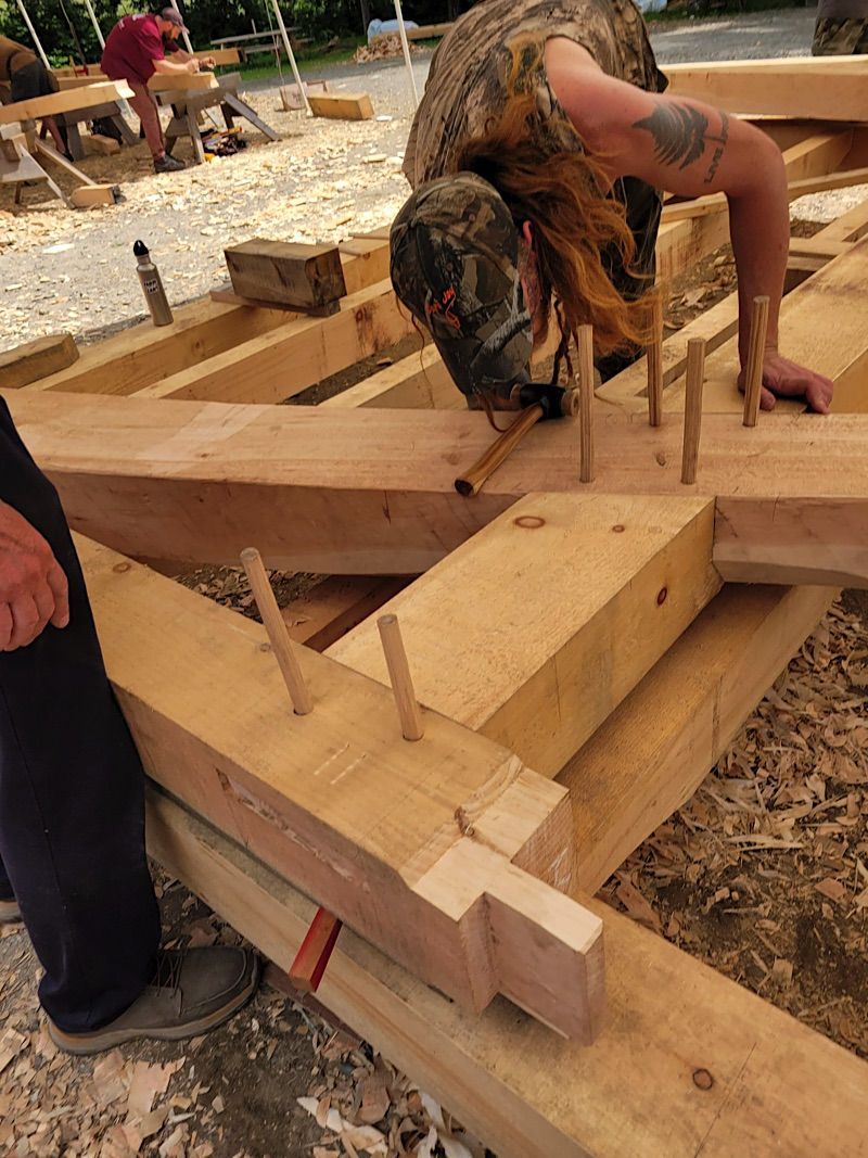 A woman working on a 16'x24' Cruck frame outside the Heartwood shop