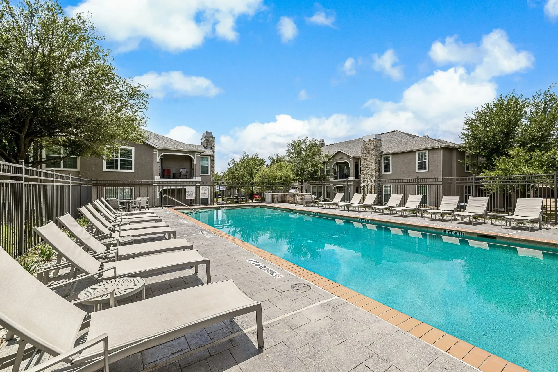 Resort-style swimming pool with lounge chairs and apartment buildings in the background.