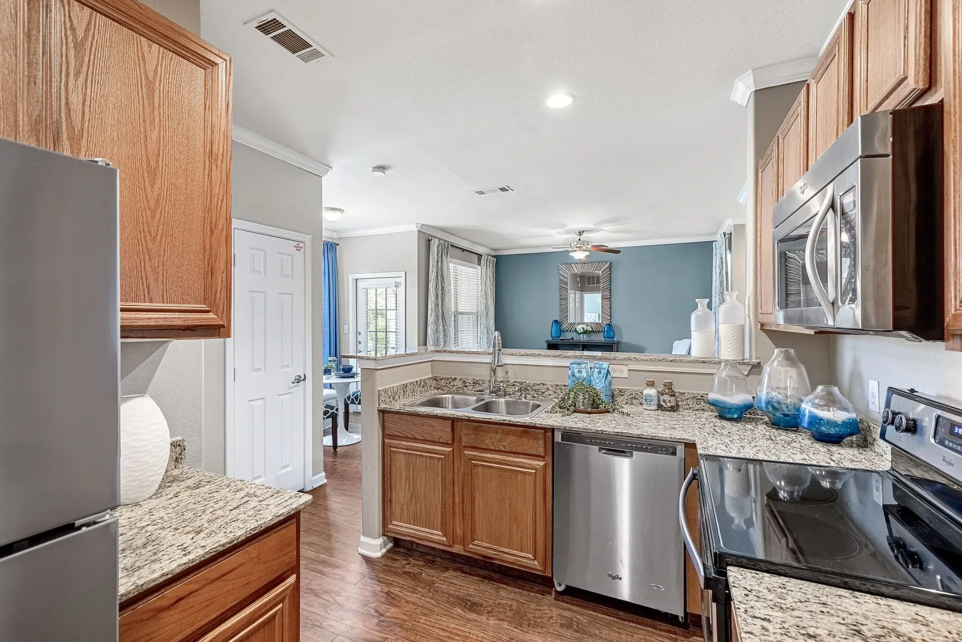 Modern kitchen with granite countertops, stainless steel appliances, and wood cabinets, open to the living room.