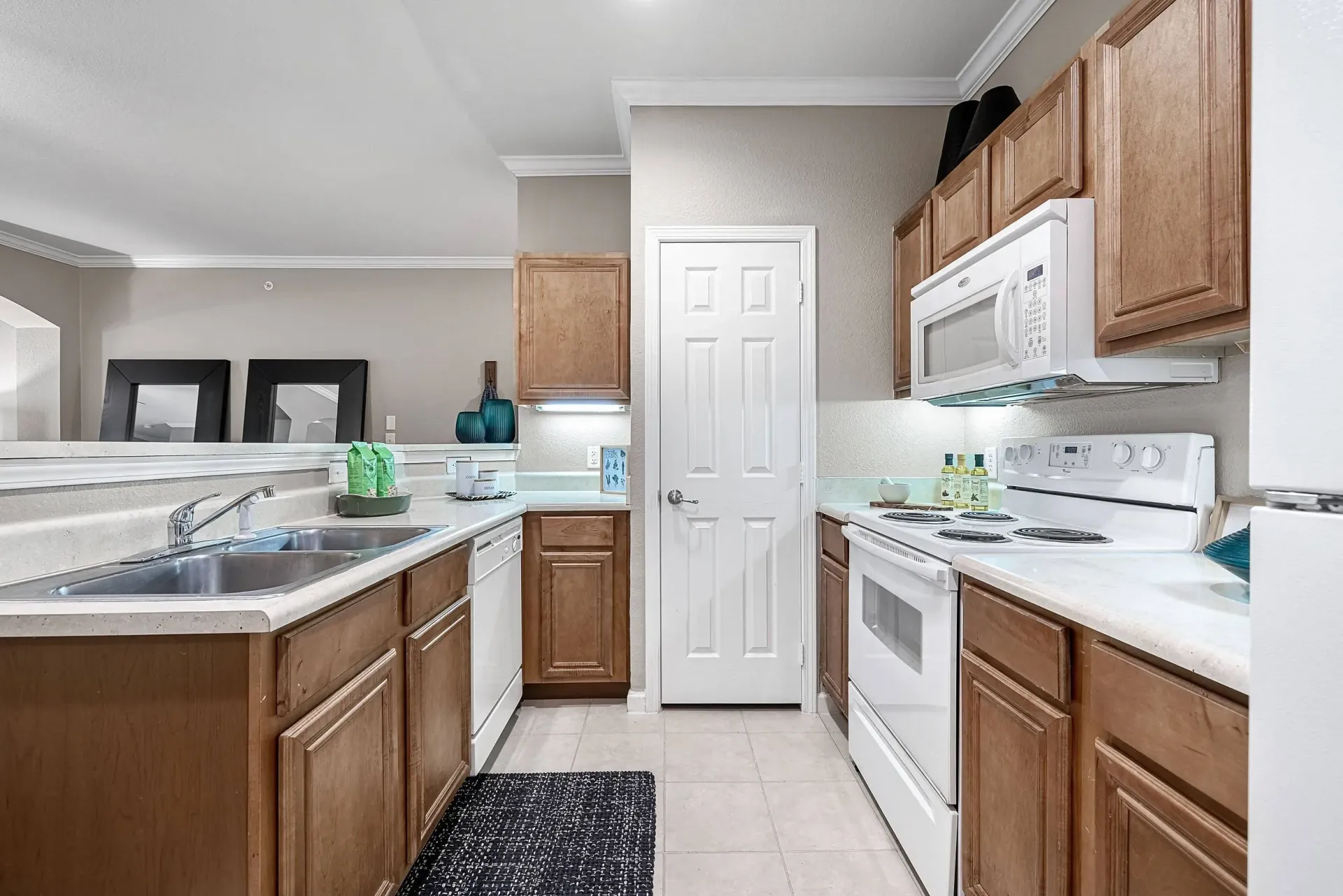 Kitchen with wood cabinets, white countertops, double sink, dishwasher, stove, and microwave.