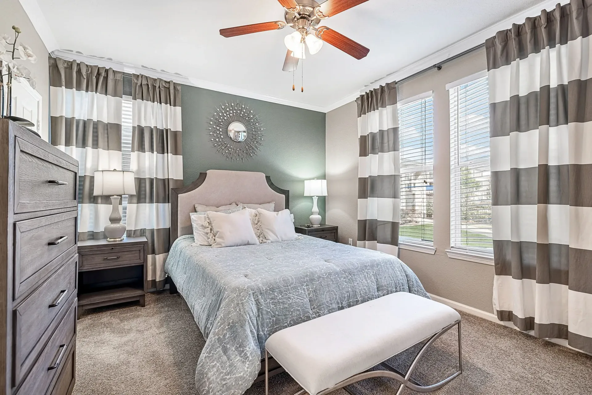 Bedroom with a king-size bed, bedside tables, dresser, and large windows with striped curtains.
