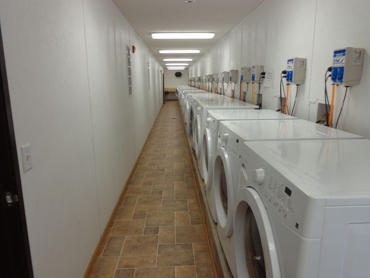 Laundry room with a row of white washers and dryers along a long tiled hallway.