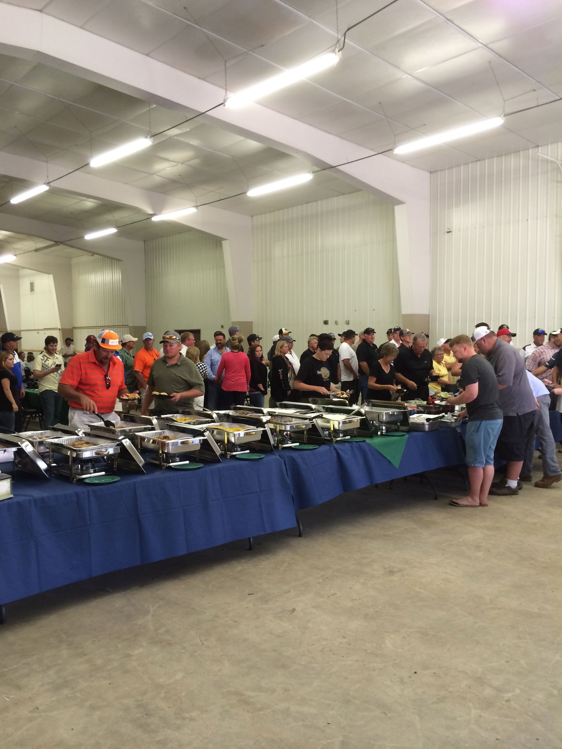 People browsing a long table of items at an indoor auction or sale, under bright warehouse lights