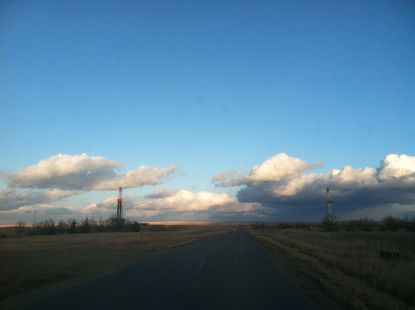 A road going through a field with clouds in the sky