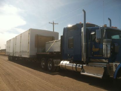 A blue semi truck is pulling a trailer on a dirt road.