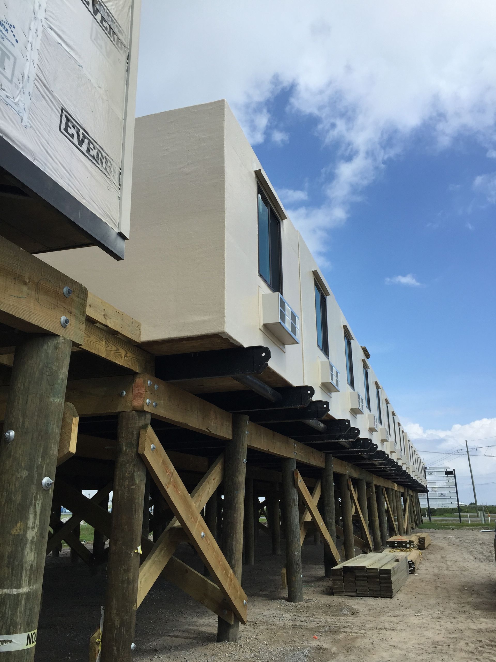 Modular houses on stilts at a construction site under a blue sky