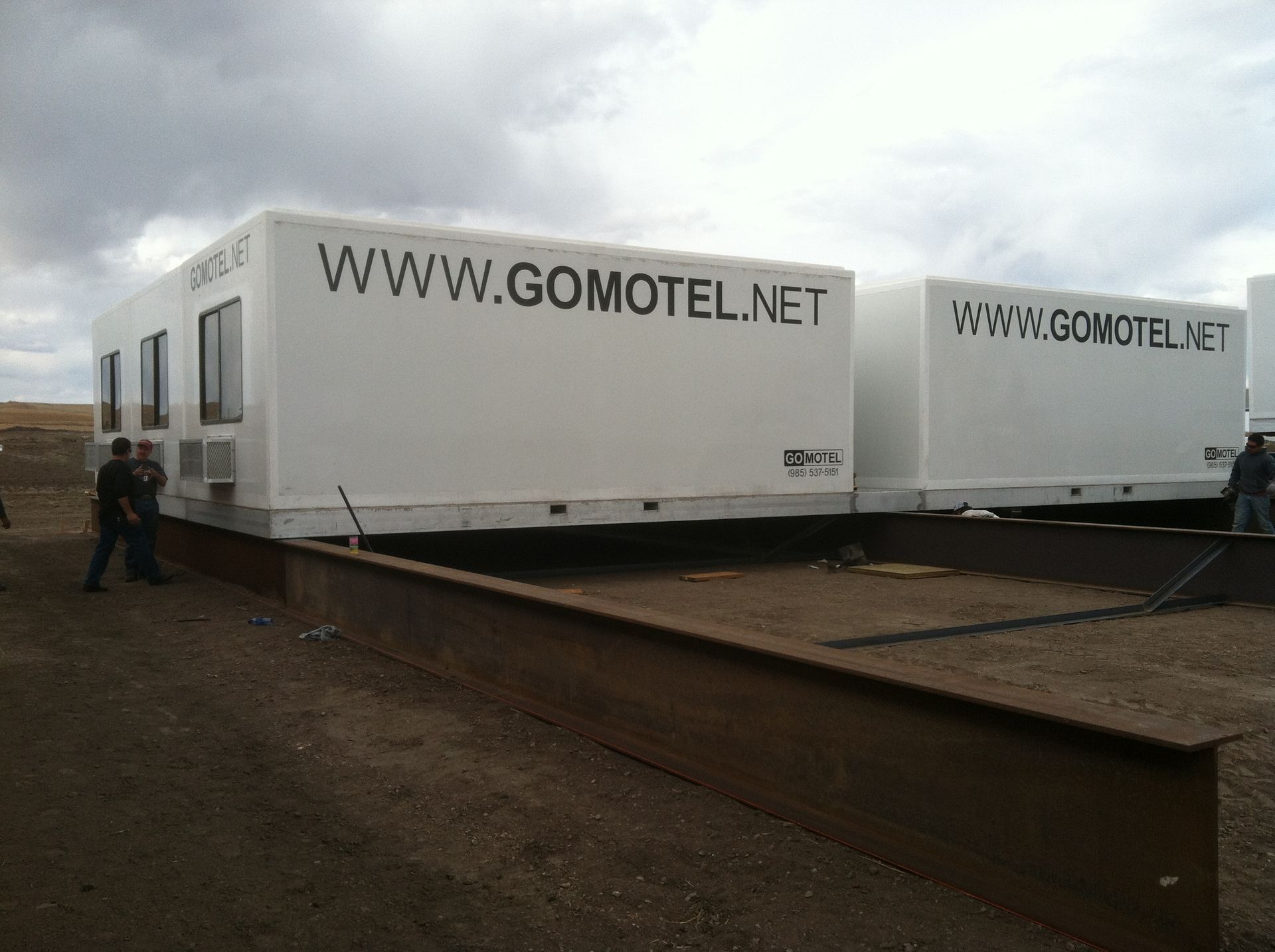 Two white GOMOTEL mobile units on a wet industrial lot under cloudy skies