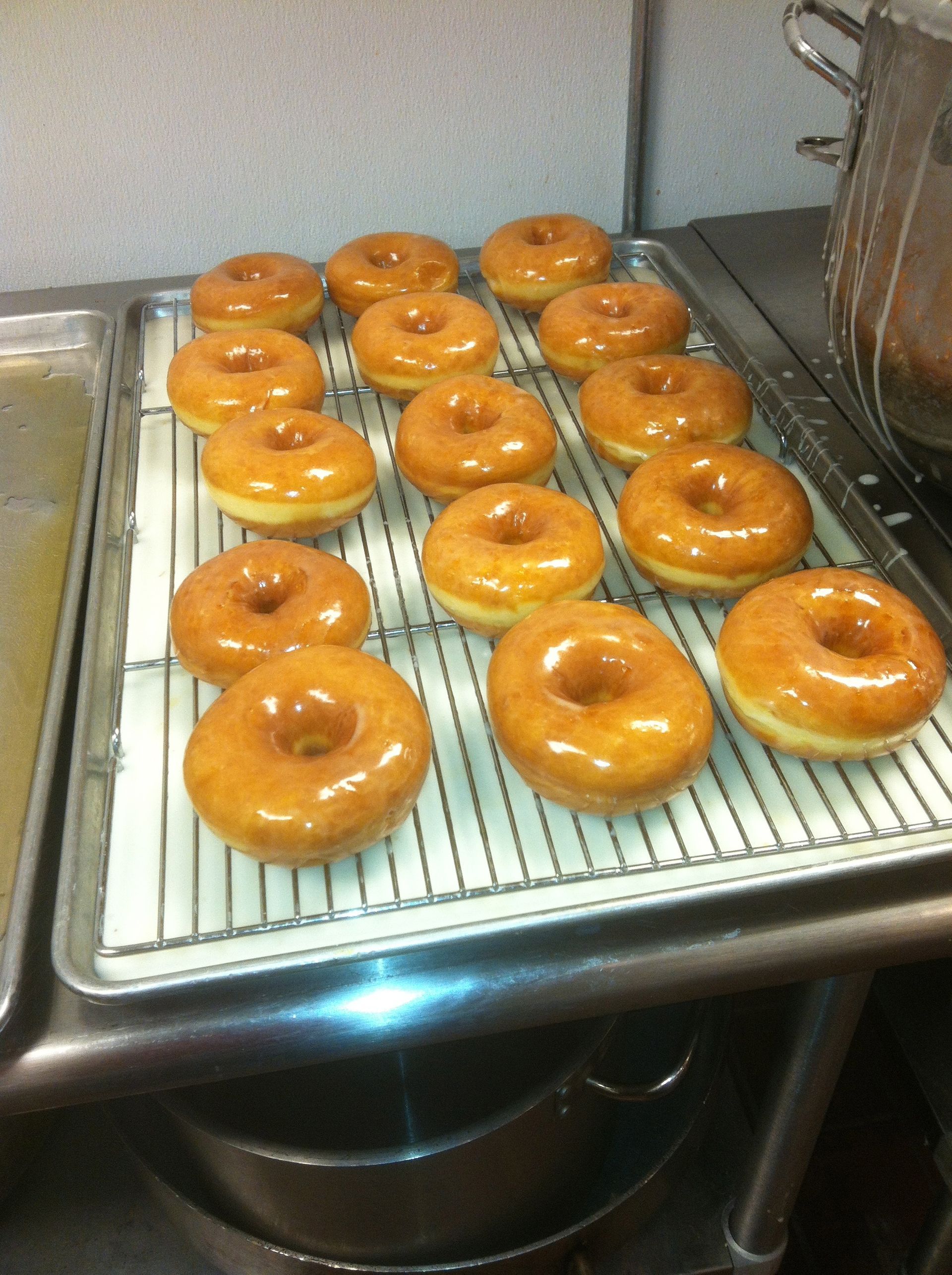 A rack of glazed donuts cooling on a wire rack in a kitchen sink area.