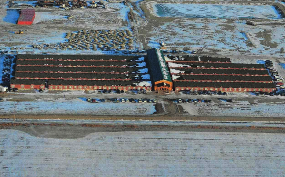 Aerial view of two long brick buildings in a snowy landscape with a road in front.