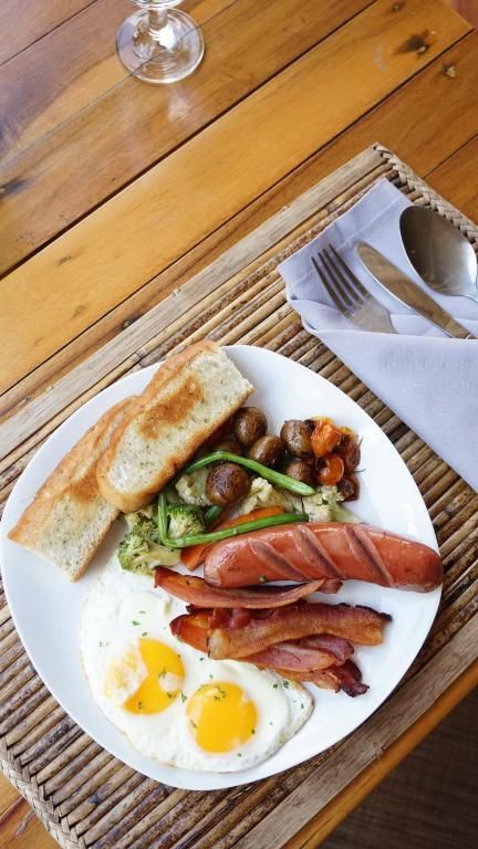 A plate of breakfast featuring fried eggs, sausage, bacon, roasted vegetables, and toasted bread on a woven mat.