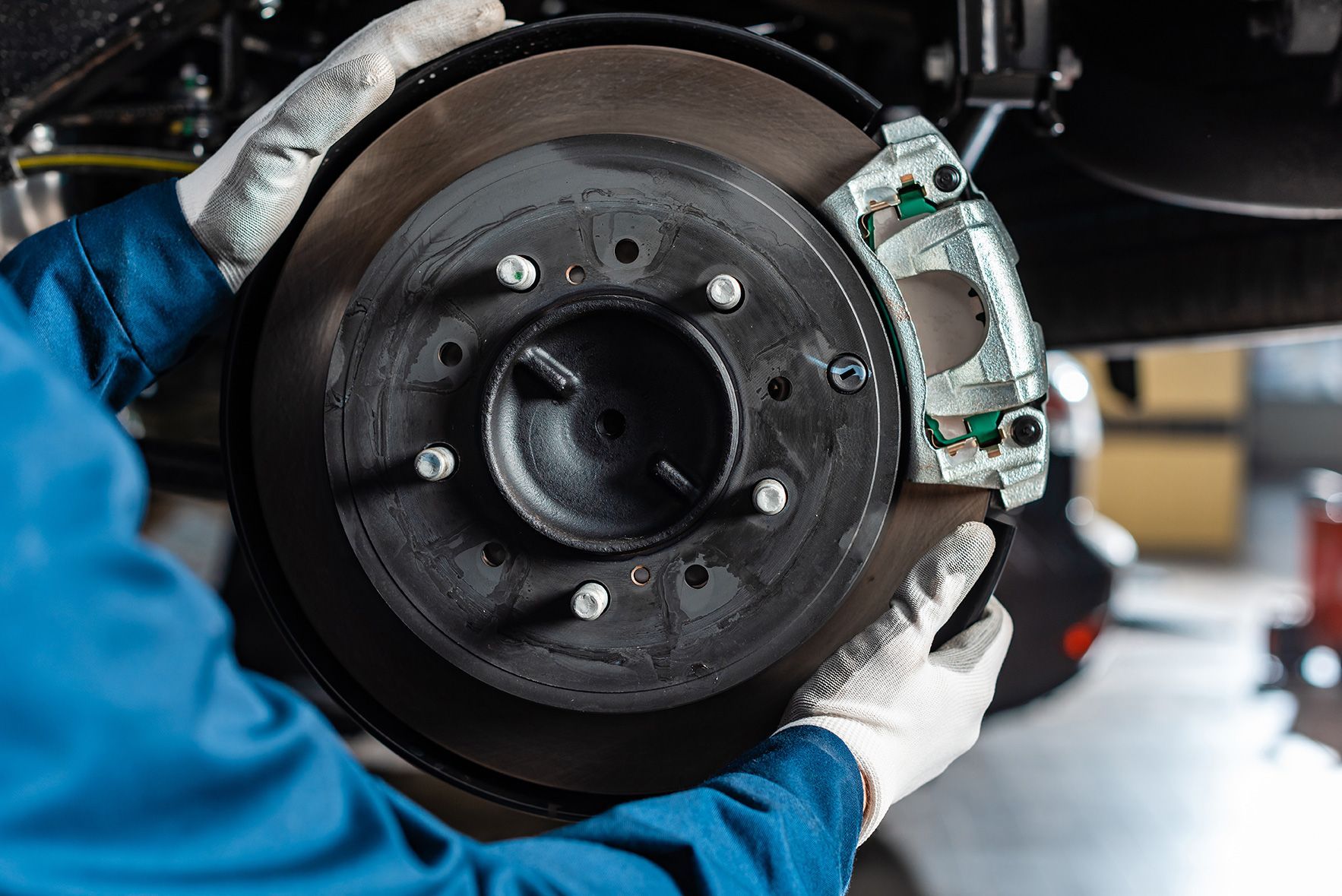 Mechanic holding car brake rotor and caliper; focus on the wheel assembly, wearing gloves.