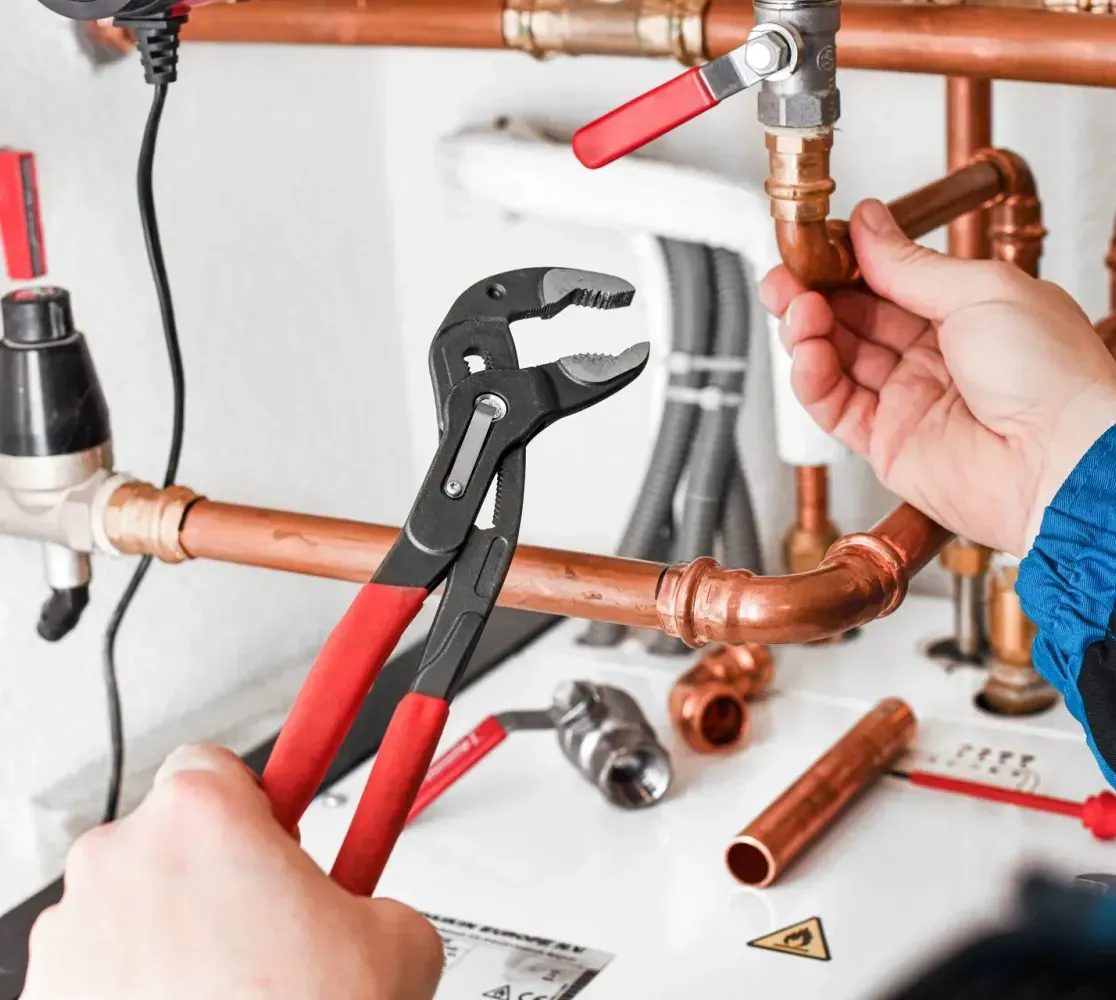 A person uses adjustable pliers to work on copper plumbing pipes in an indoor setting.