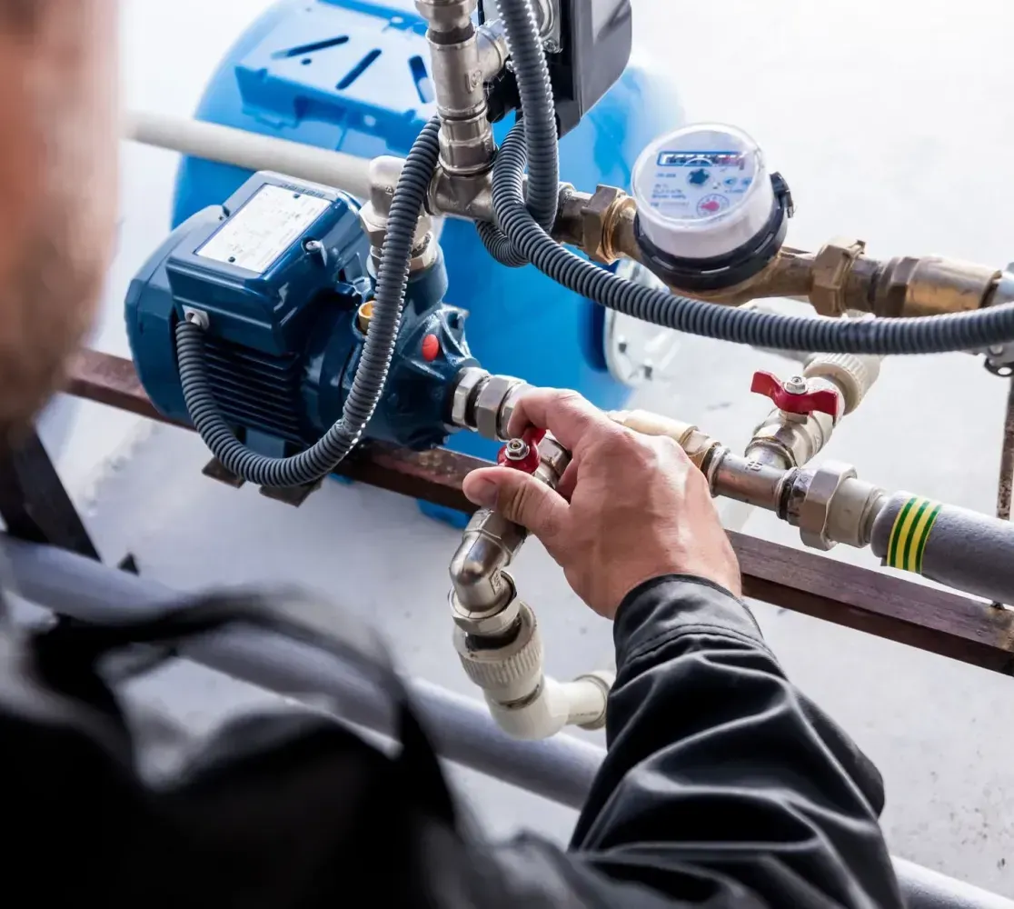 A person adjusts a valve on a blue water pump and piping system.